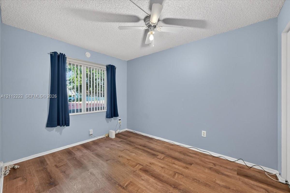 Wood-finish flooring, textured ceiling, central ceiling fan with integrated lighting, and horizontal blinds