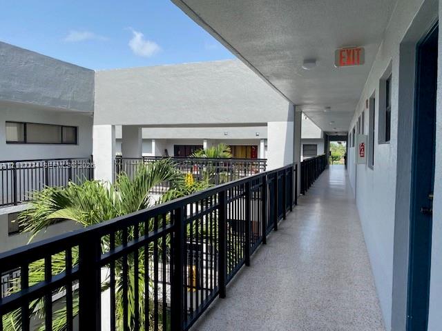 Open-air walkway featuring speckled concrete flooring, matte black metal railings, and stucco exterior walls