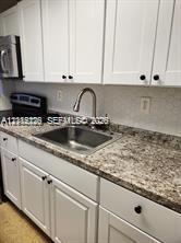 Kitchen featuring white shaker-style cabinetry, stone-finish countertops, stainless steel undermount sink, gooseneck faucet, and built-in appliances