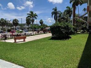 Common area grounds featuring manicured turf, mature palm trees, decorative shrubbery, and a paved walkway with a built-in bench
