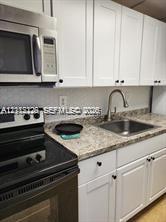 Kitchen featuring white shaker-style cabinetry, stone-patterned laminate countertops, a stainless steel undermount sink with a gooseneck faucet, and stainless steel built-in appliances