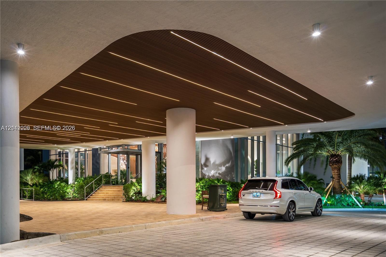 Covered porte-cochre featuring a linear wood-slat ceiling, integrated LED recessed lighting, structural support columns, and paved motor court