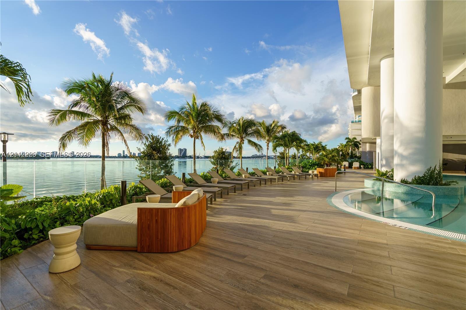 Pool deck featuring tile flooring, a curvilinear built-in spa with tile surround, glass railings, and mature palm trees