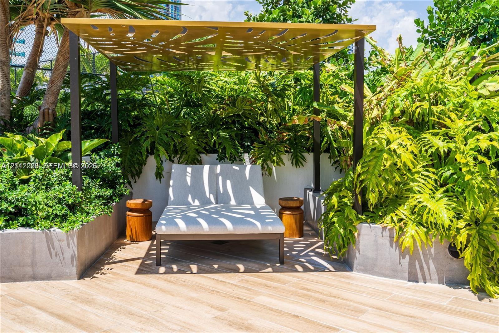Outdoor terrace featuring wood-finish tile flooring, a custom metal pergola with laser-cut decorative detailing, and integrated concrete planters with mature landscaping