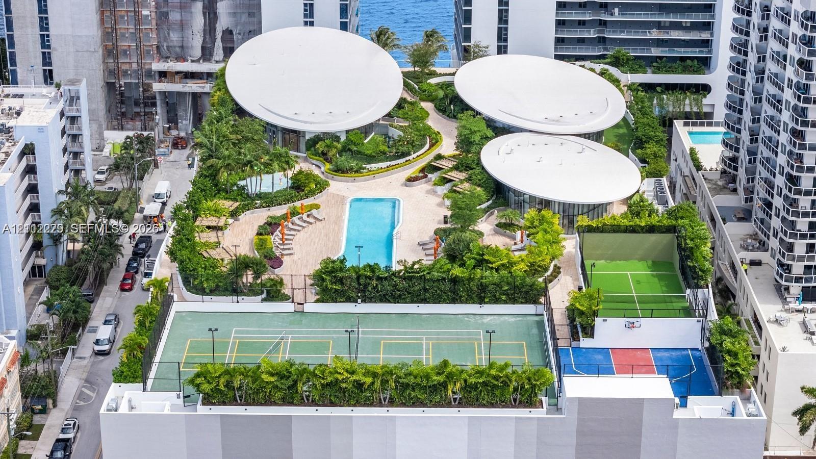 Elevated amenity deck featuring a swimming pool, tennis court, multi-sport court, landscaped green spaces, and distinctive modern architectural structures