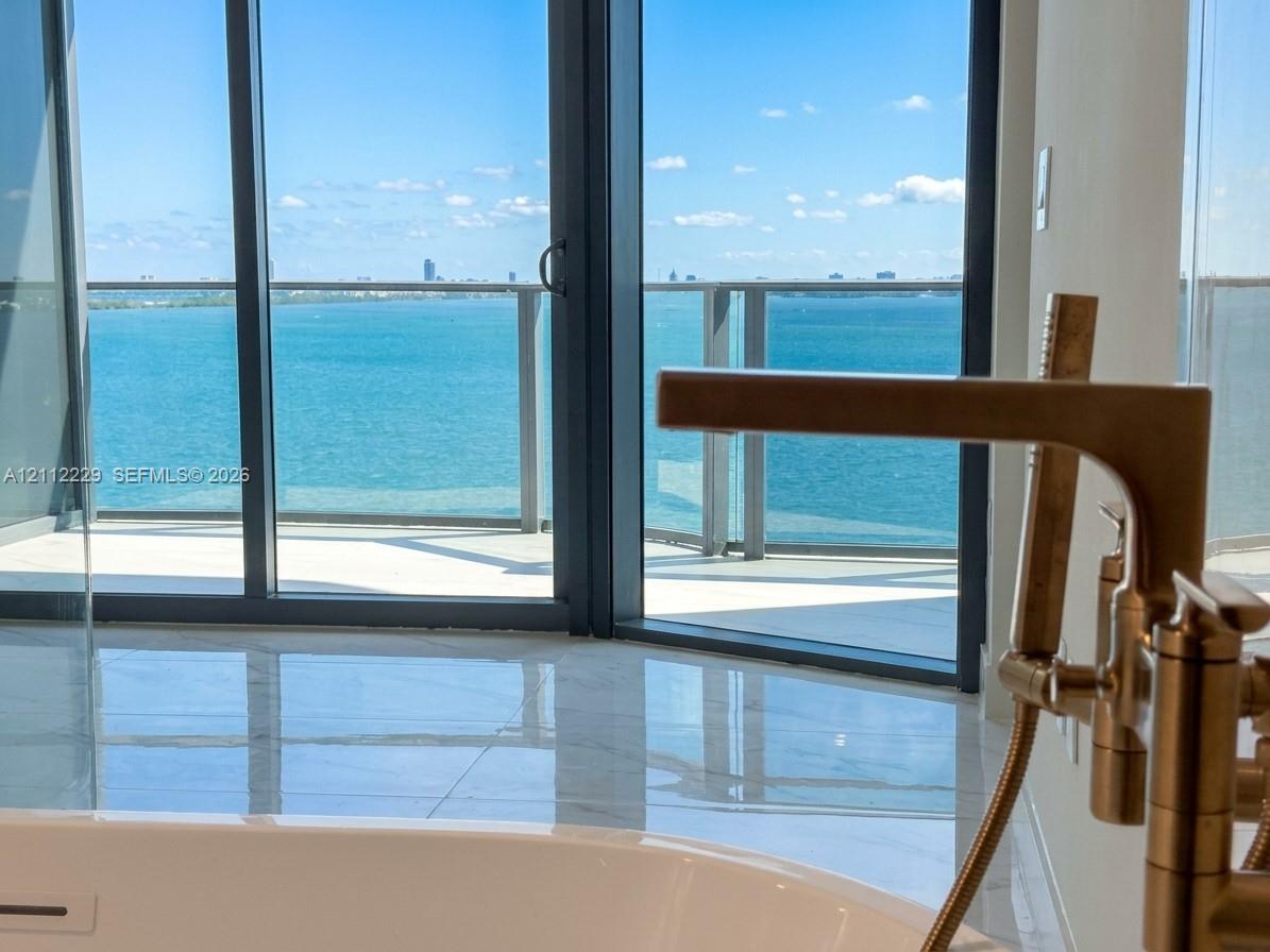 Soaking tub with a metallic floor-mounted faucet, expansive floor-to-ceiling windows, and a private balcony featuring a glass railing