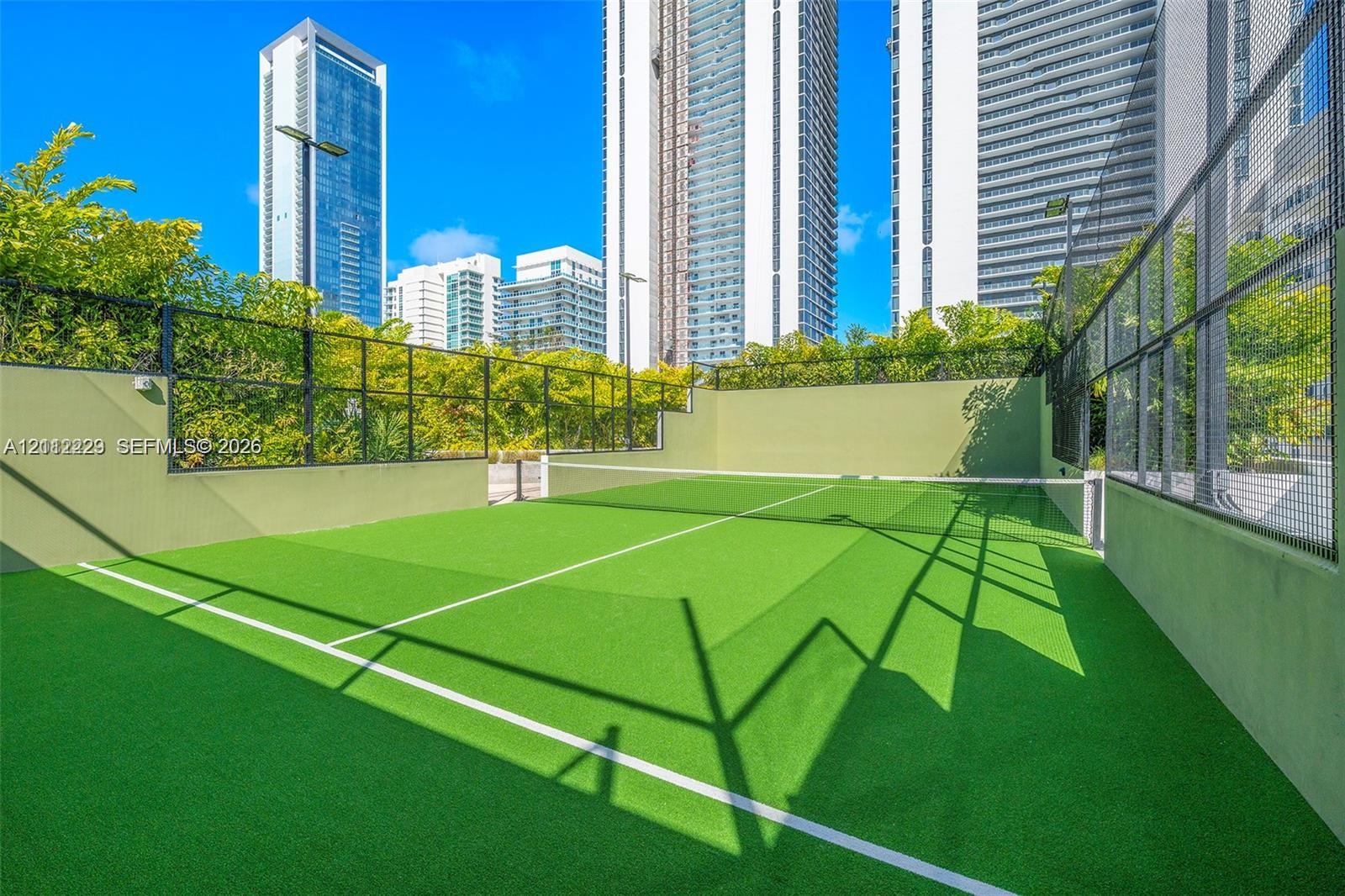 Outdoor athletic court featuring synthetic turf surfacing, perimeter fencing, and concrete boundary walls