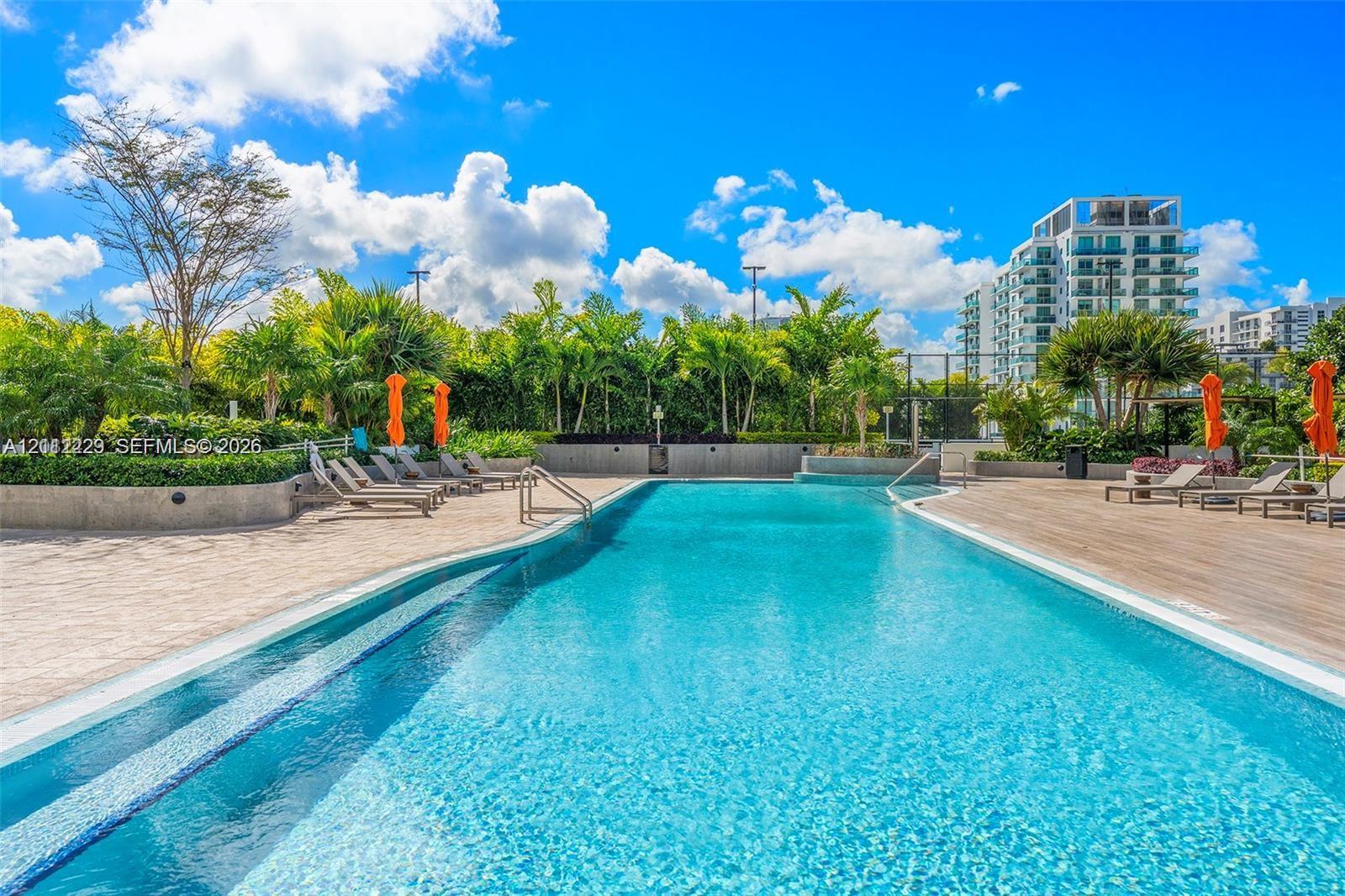 Swimming pool with integrated steps, tile decking, stone retaining walls, and surrounding mature palm trees