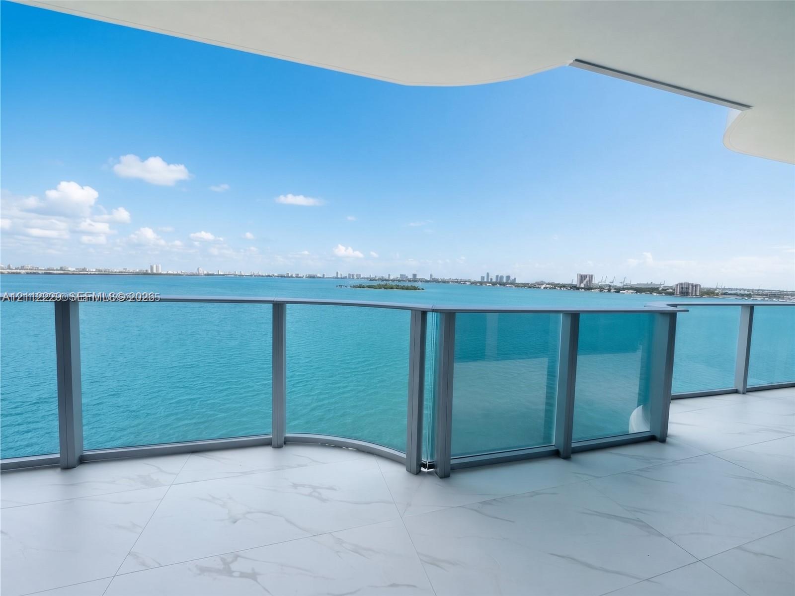 Expansive covered balcony featuring white tiled flooring and a glass panel railing overlooking the water