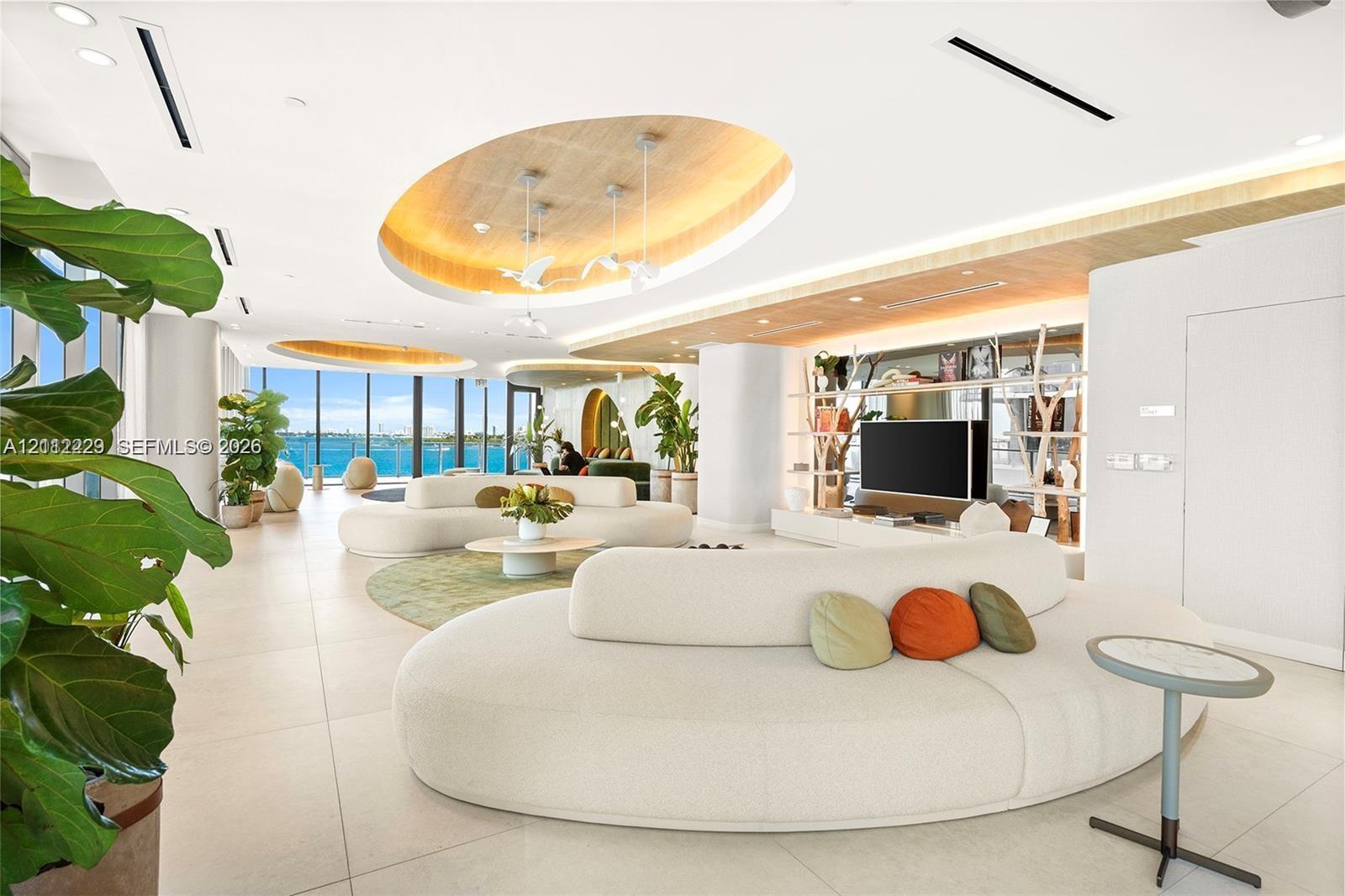 Open-concept living space featuring tile flooring, recessed oval tray ceilings with warm lighting, floor-to-ceiling windows, and built-in shelving with integrated lighting