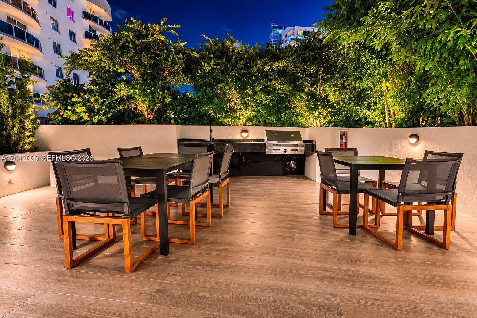 Outdoor terrace featuring wood-finish tile flooring, built-in stainless steel grill, solid surface countertop, wall-mounted light fixtures, and perimeter privacy walls