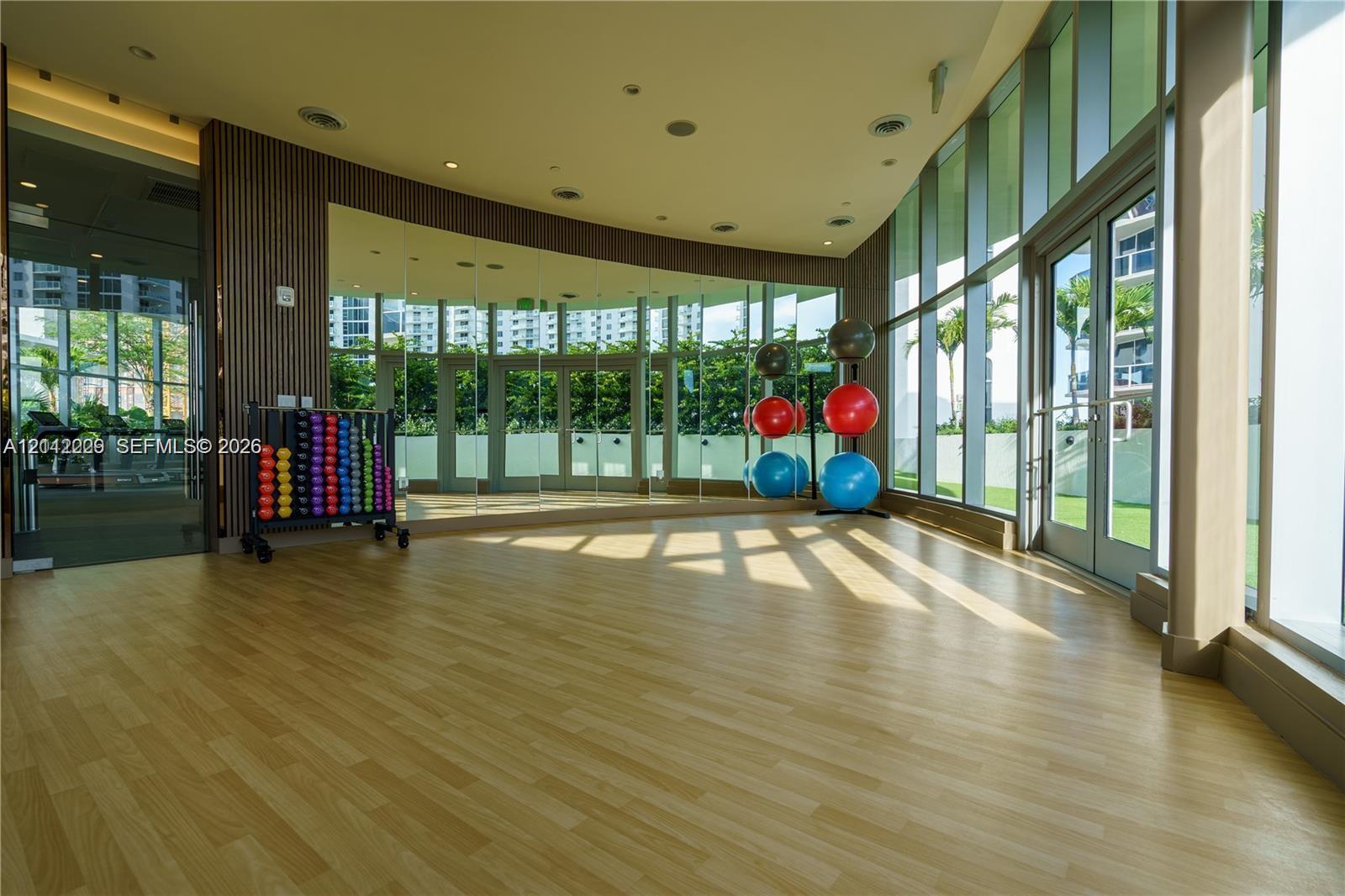Wood-finish flooring, full-wall mirrors, floor-to-ceiling glass paneling, vertical wood slat accent wall, and recessed ceiling lighting