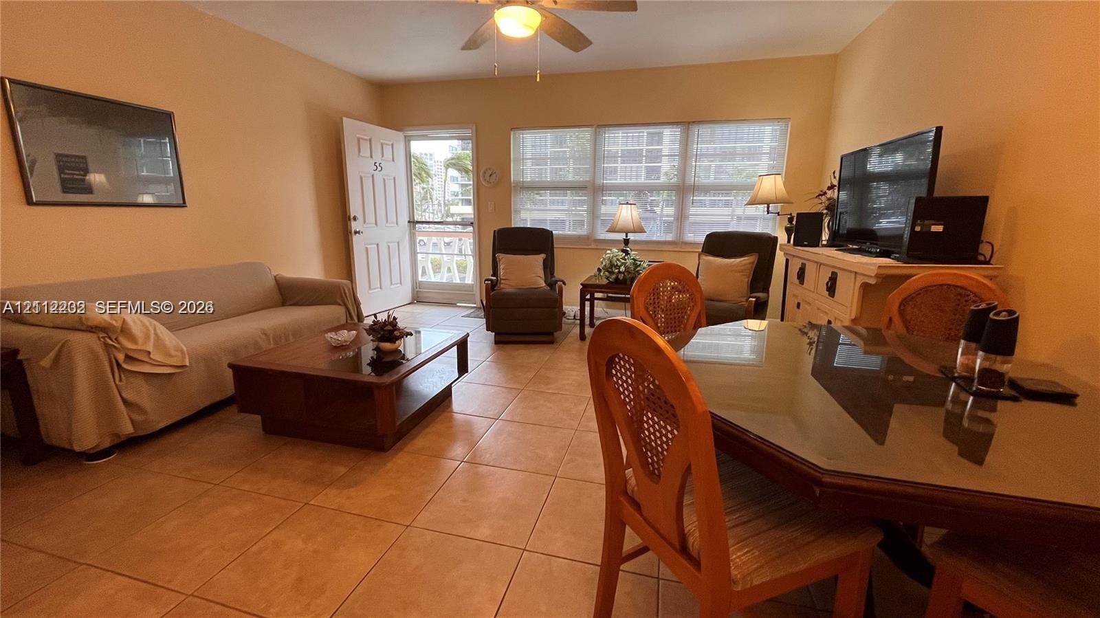 Neutral tile flooring, multiple windows providing natural illumination, ceiling fan, and entry door with screen