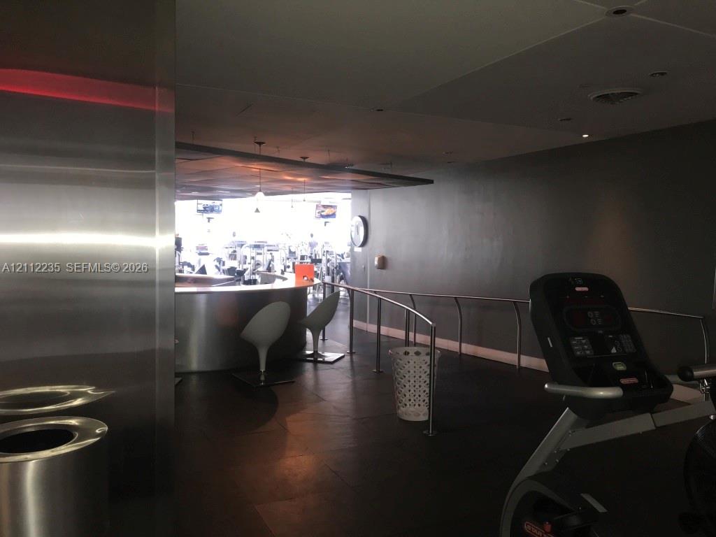 Fitness area featuring dark tile flooring, a curved stainless steel bar, recessed ceiling lighting, and metal handrails
