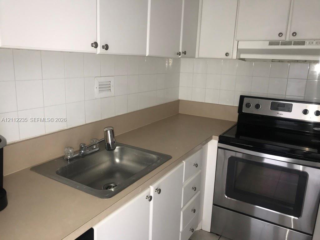 Kitchen featuring white cabinetry, solid surface countertops, stainless steel electric range, square-tile backsplash, and drop-in sink with dual-handle faucet