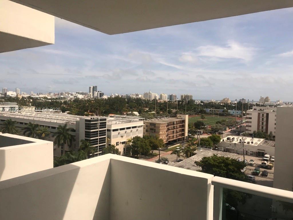 Private concrete balcony featuring a metal and glass railing, providing an elevated perspective of the surrounding cityscape