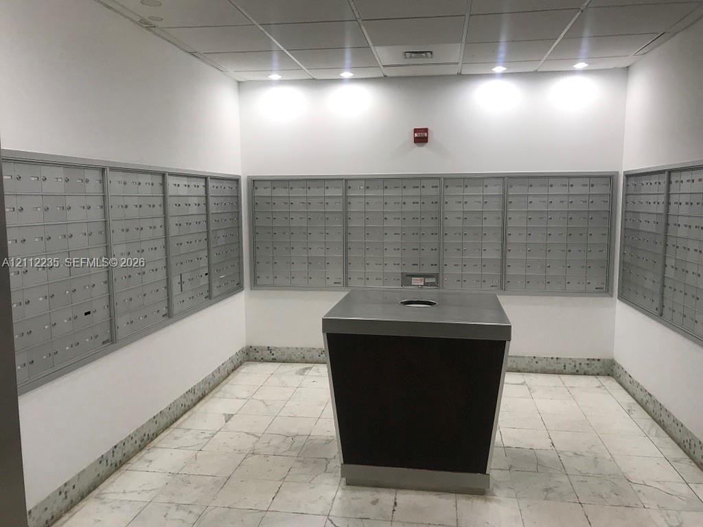 Mail room featuring multiple banks of wall-mounted metal mailboxes, central parcel station with stone countertop, recessed lighting, and stone flooring