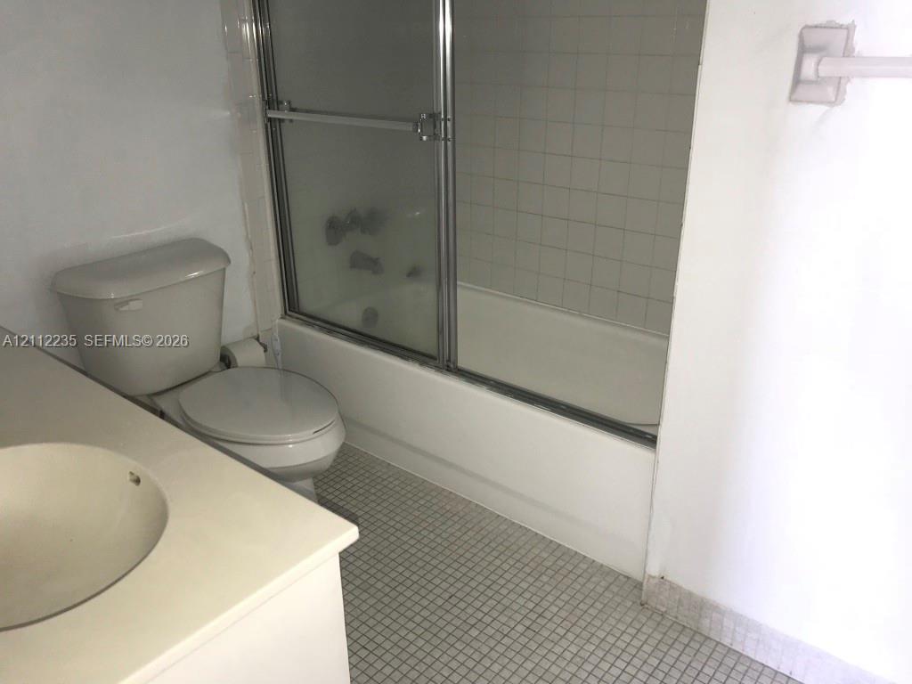 Bathroom featuring a vanity with an integrated sink, bathtub with a sliding glass enclosure, tile wall surround, and tiled flooring