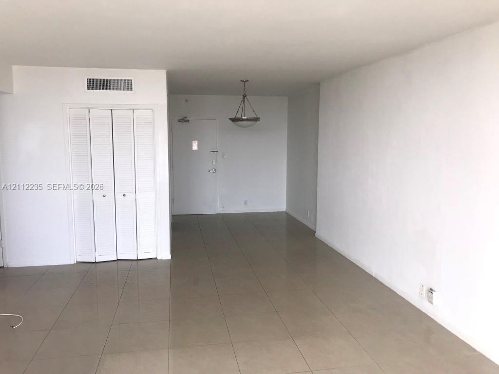 Large-format tile flooring, louvered bi-fold closet doors, and a decorative pendant light fixture