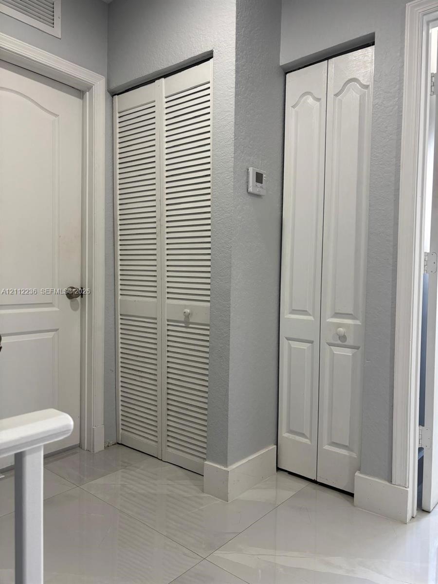 Neutral interior featuring large-format ceramic tile flooring, white six-panel door, louvered double-door storage, and a paneled bifold door