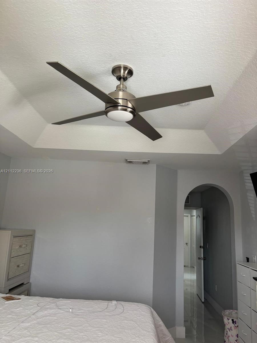 Tray ceiling featuring a brushed nickel four-blade ceiling fan with an integrated light fixture and a structural arched doorway