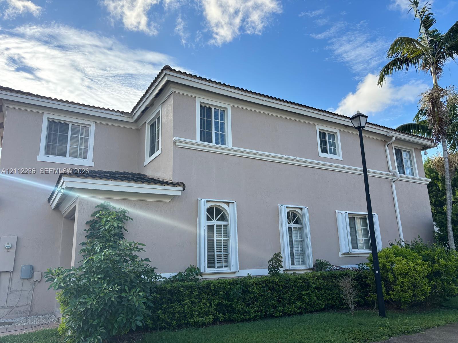 Two-story stucco exterior featuring arched windows, multi-pane glass, tiled roofline, and manicured landscaping