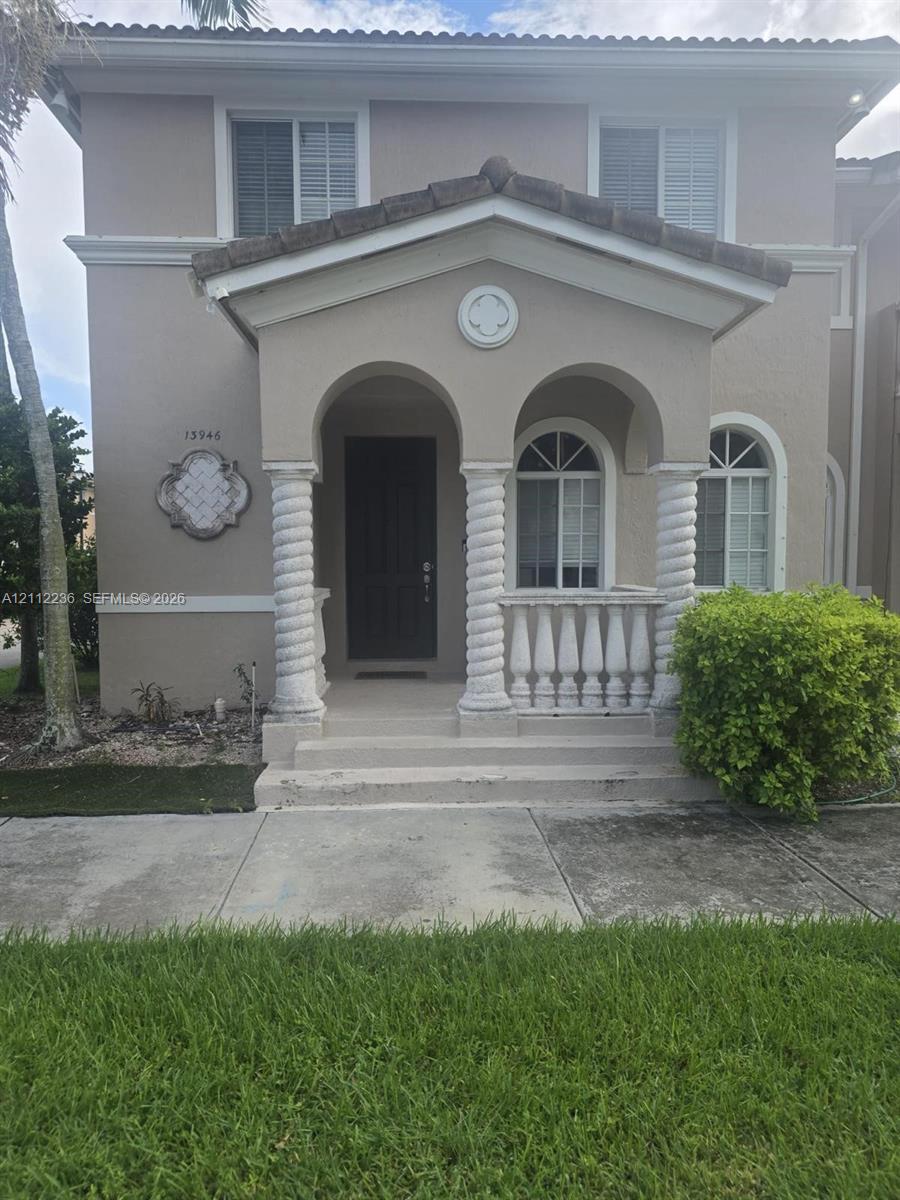 Two-story exterior featuring a covered front porch with spiral columns, decorative stone balustrade, arched window casings, and a tiled gable roof