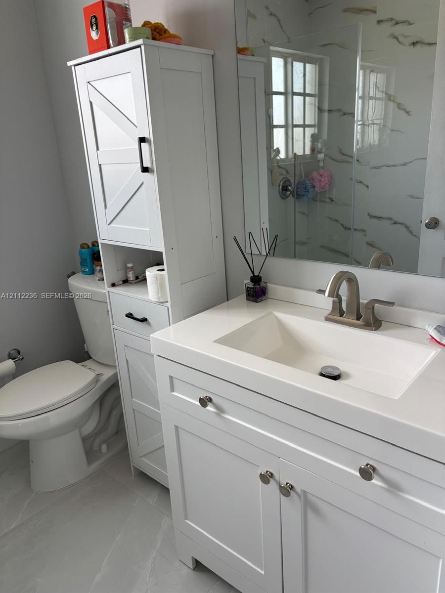 Bathroom featuring a white vanity with an integrated basin, quartz-style countertop, tall built-in storage cabinetry with matte black hardware, and large-format tile flooring
