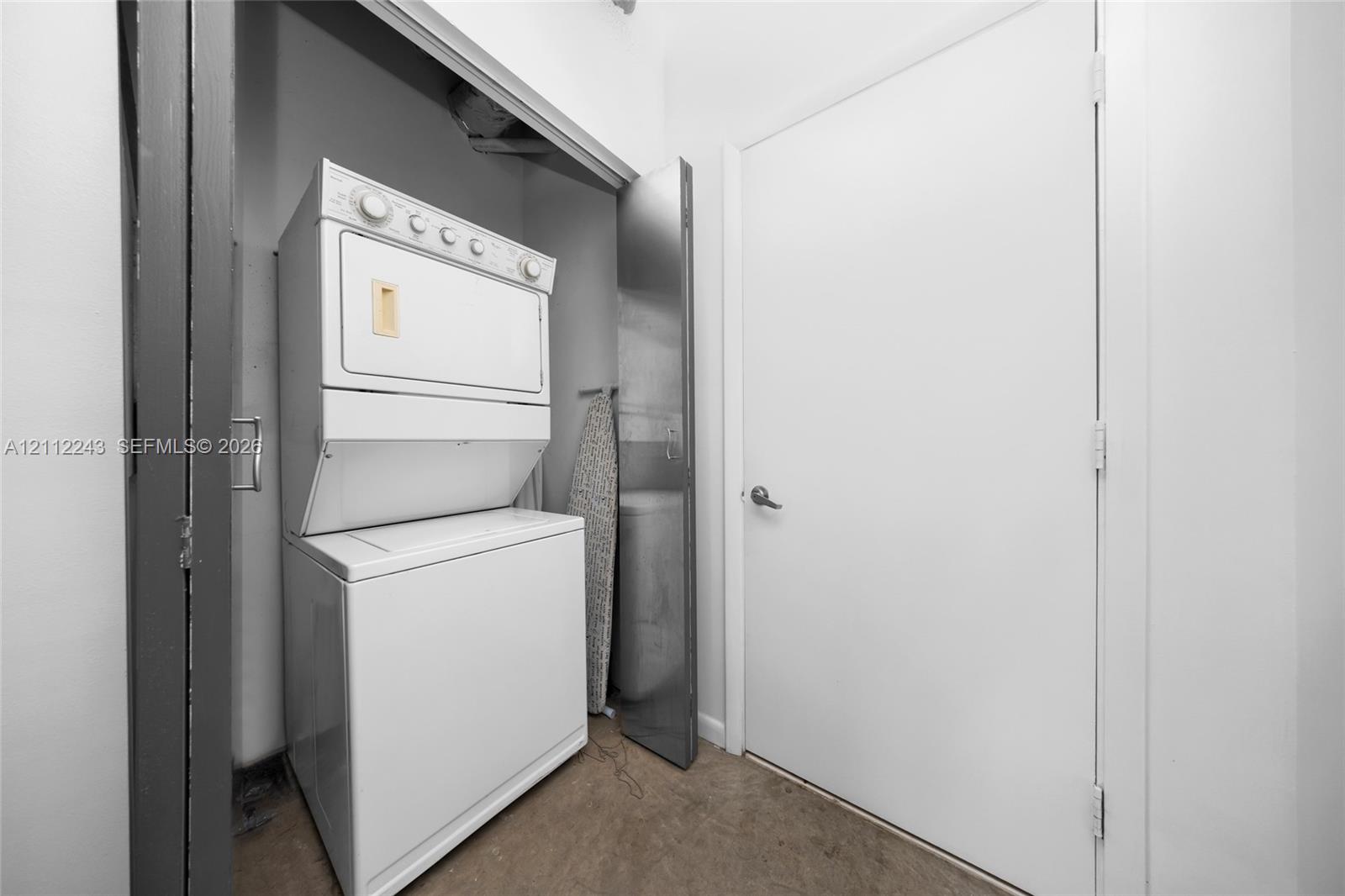 Laundry closet featuring a stackable white washer and dryer unit, solid-core white door, and neutral flooring