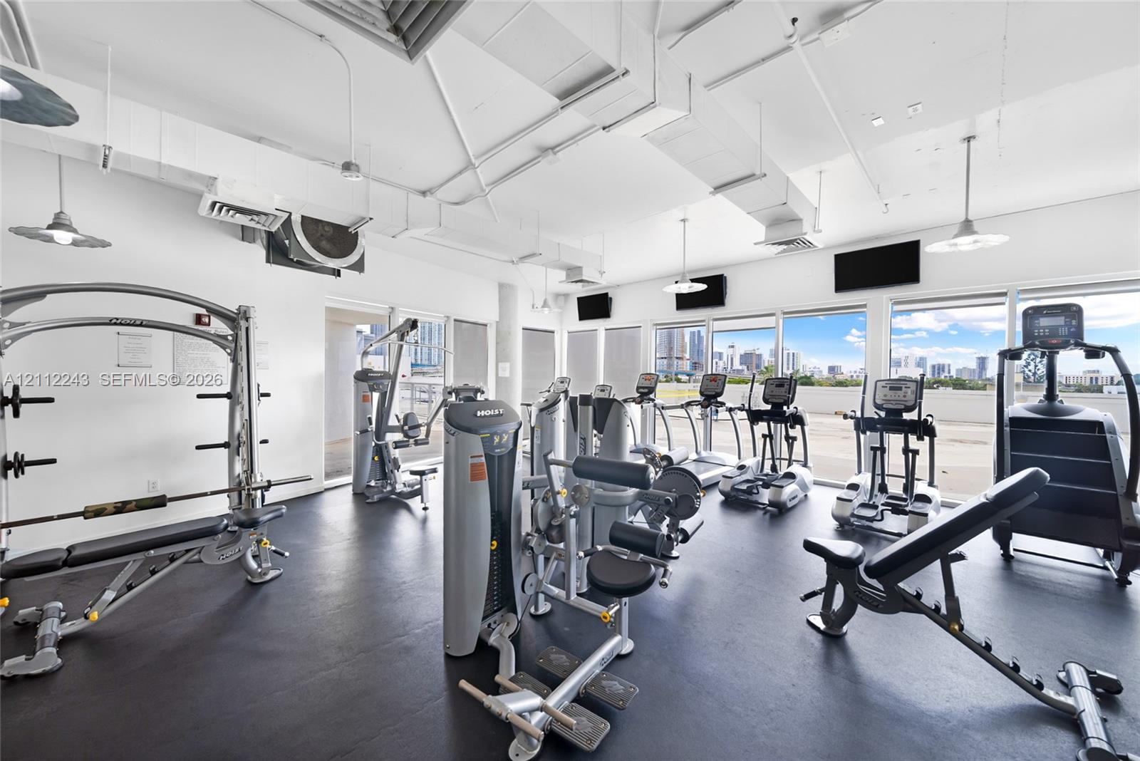 Fitness facility featuring industrial-style exposed ductwork, rubberized flooring, and expansive floor-to-ceiling windows