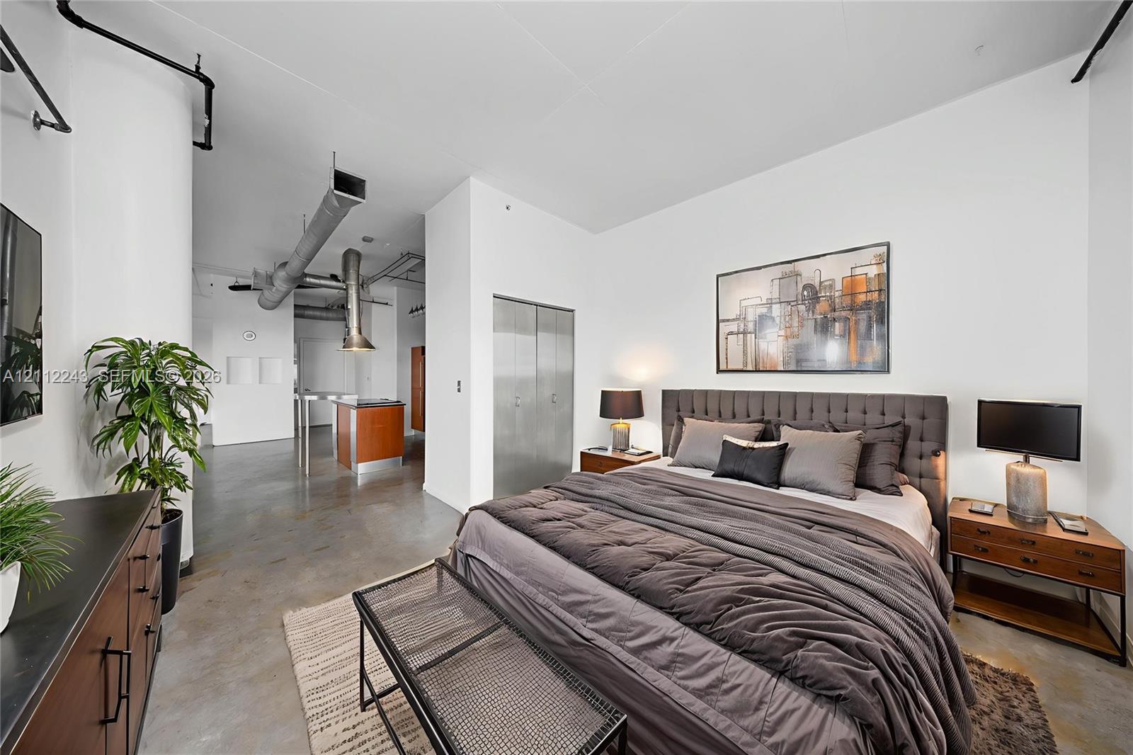 Industrial-style loft featuring exposed overhead ductwork, polished concrete flooring, soaring ceilings, and metal-clad closet doors