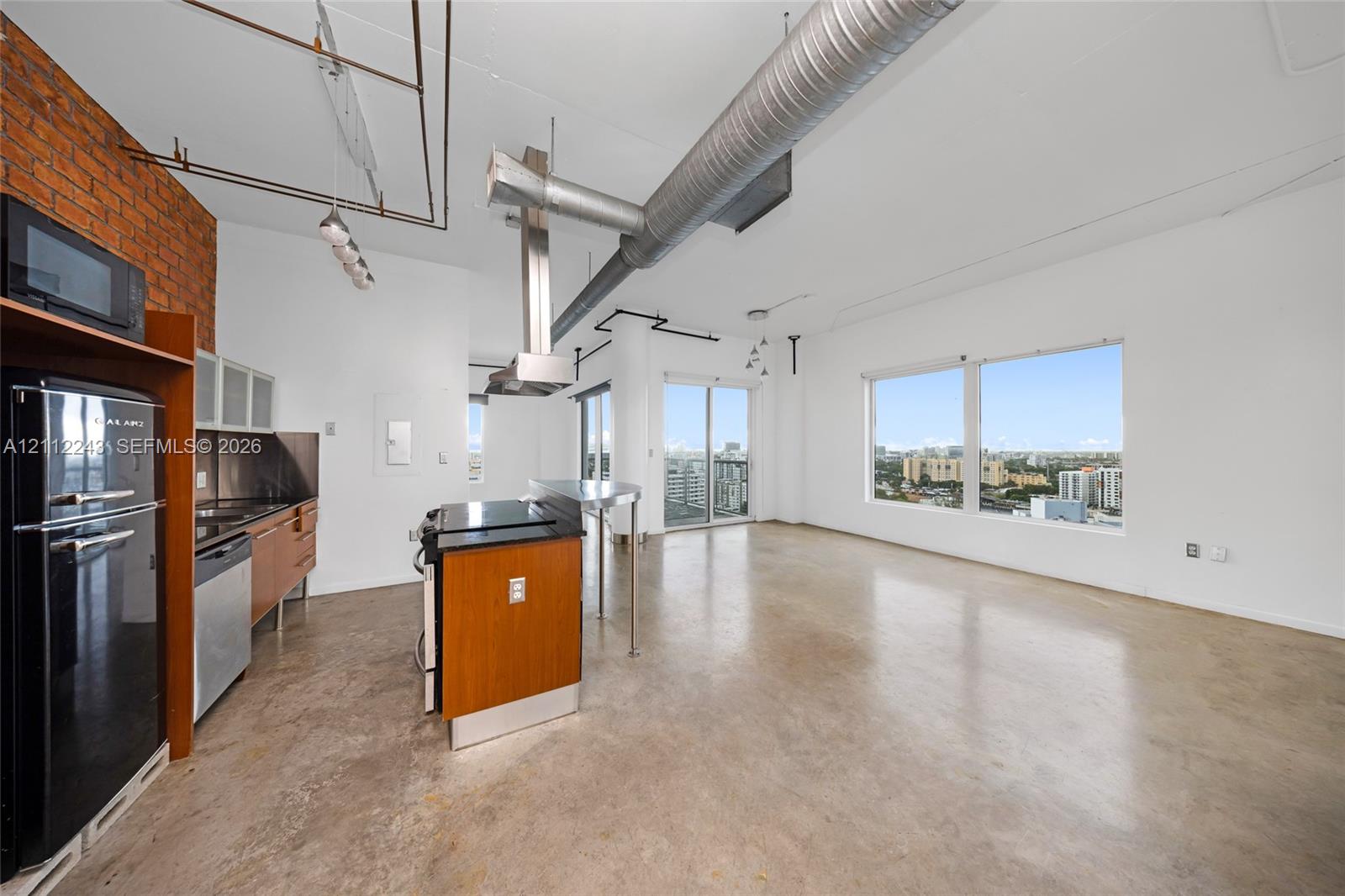 Exposed brick wall, polished concrete flooring, stainless steel range hood, built-in cabinetry, and large multi-pane windows