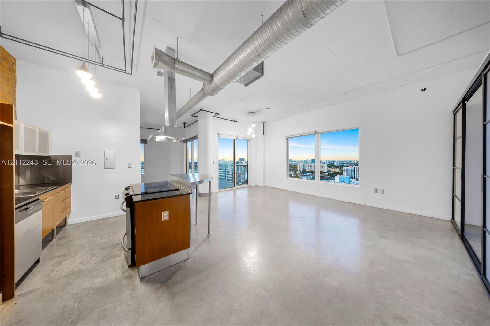 Open-concept industrial-style interior featuring polished concrete flooring, exposed overhead ductwork, floor-to-ceiling windows, and cabinetry with stainless steel appliances