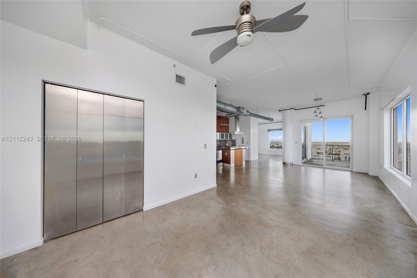 Polished concrete flooring, floor-to-ceiling metal-clad closet doors, industrial-style exposed ductwork, and sliding glass doors with exterior balcony access