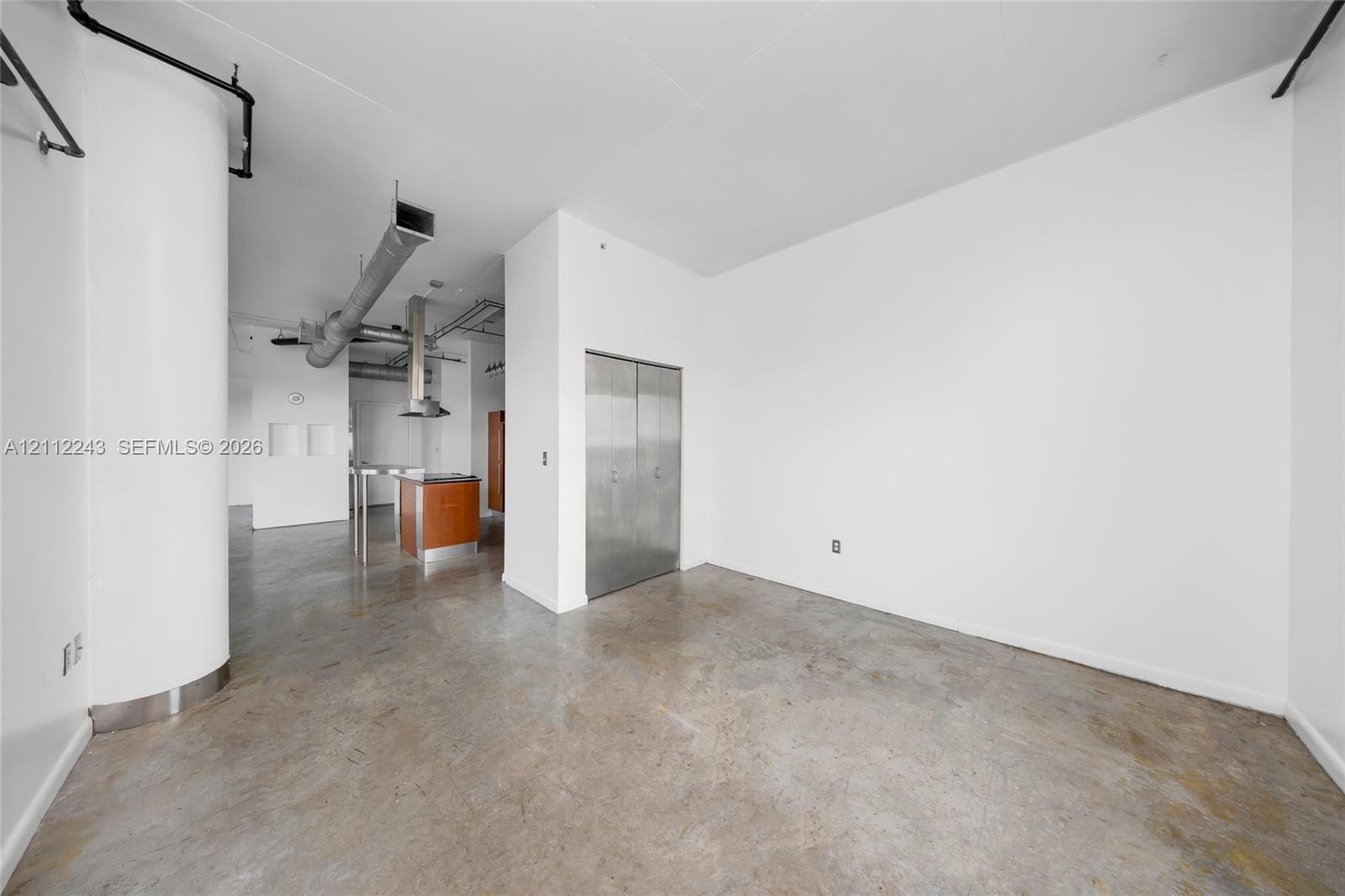 Industrial-style interior featuring polished concrete flooring, exposed overhead ductwork, a curved architectural column, and stainless steel closet doors