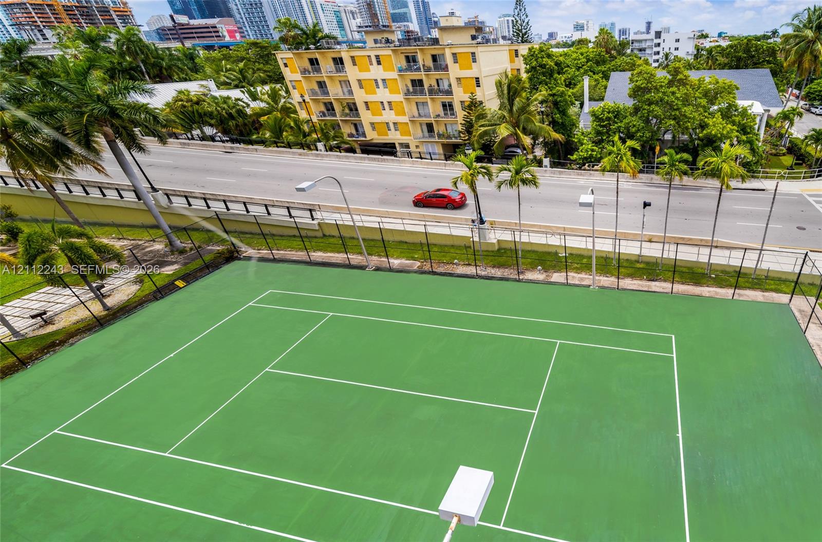Tennis court featuring a paved surface, perimeter chain-link fencing, and exterior floodlighting