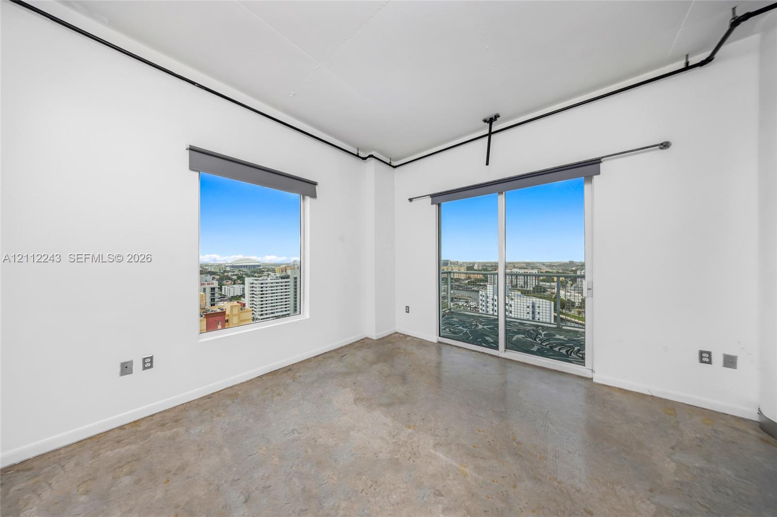 Polished concrete flooring, floor-to-ceiling window, glass sliding door, metal balcony railing, and exposed ceiling conduit