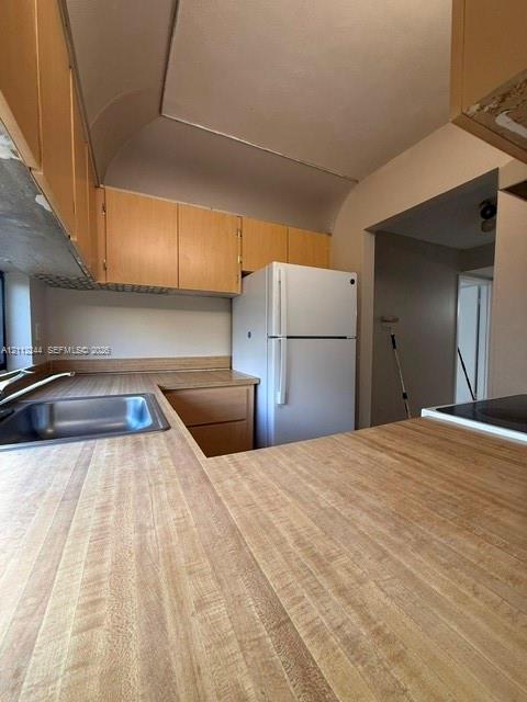 Kitchen featuring wood-finish cabinetry, neutral countertops, a stainless steel sink, and a built-in refrigerator