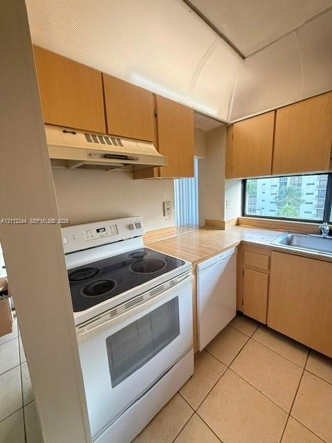 Kitchen featuring wood-finish cabinetry, solid-surface countertops, tile flooring, and integrated white appliances including an electric range and dishwasher