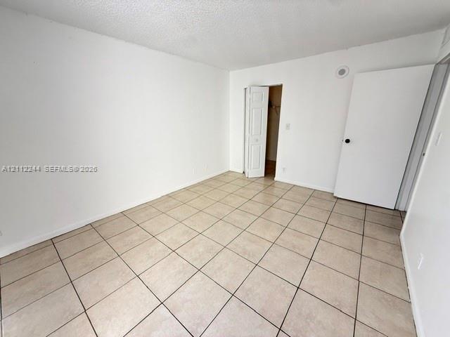 Neutral-toned floor tiling, textured ceiling, solid core swing door, and bifold closet door