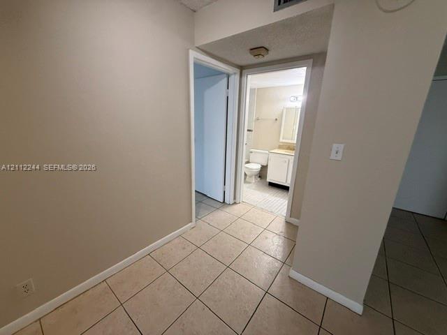 Neutral tile flooring, interior doors with white trim, and a built-in bathroom vanity with a basin sink