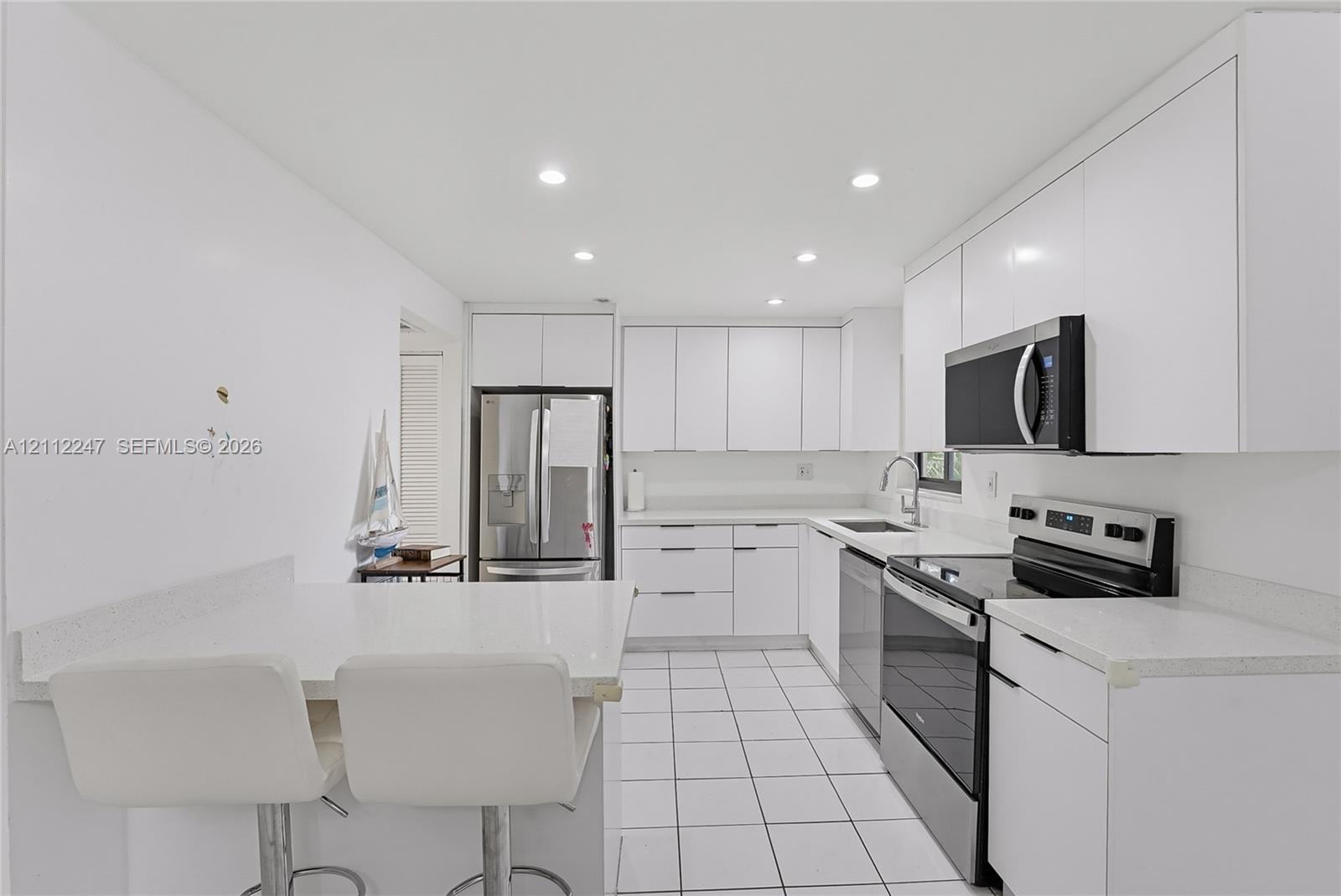 Kitchen featuring white cabinetry, solid-surface countertops, tile flooring, stainless steel appliances, and recessed lighting