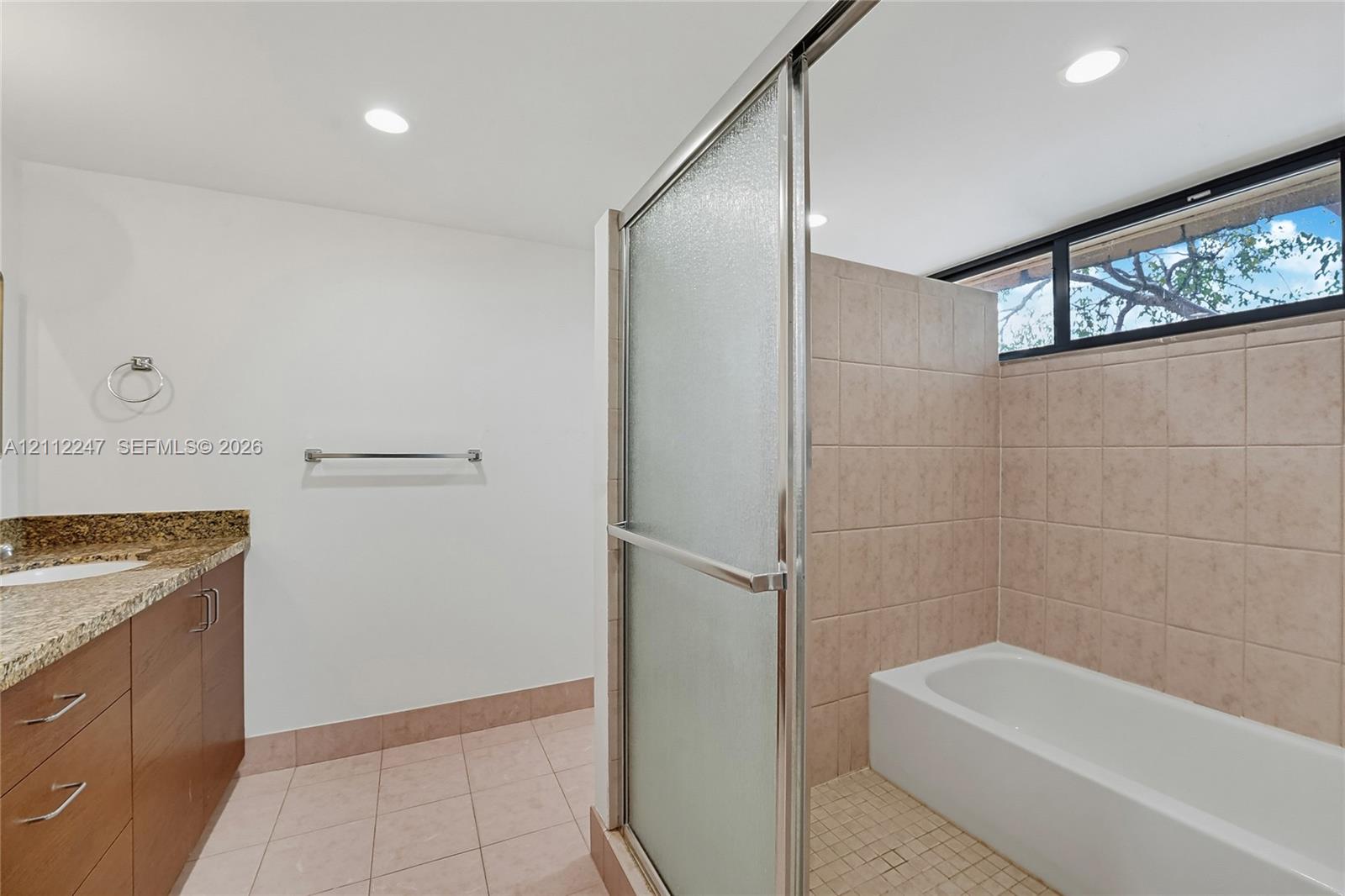Bathroom featuring a vanity with stone-finish countertop, tiled shower-tub combination with sliding glass doors, horizontal clerestory window, and recessed ceiling lighting