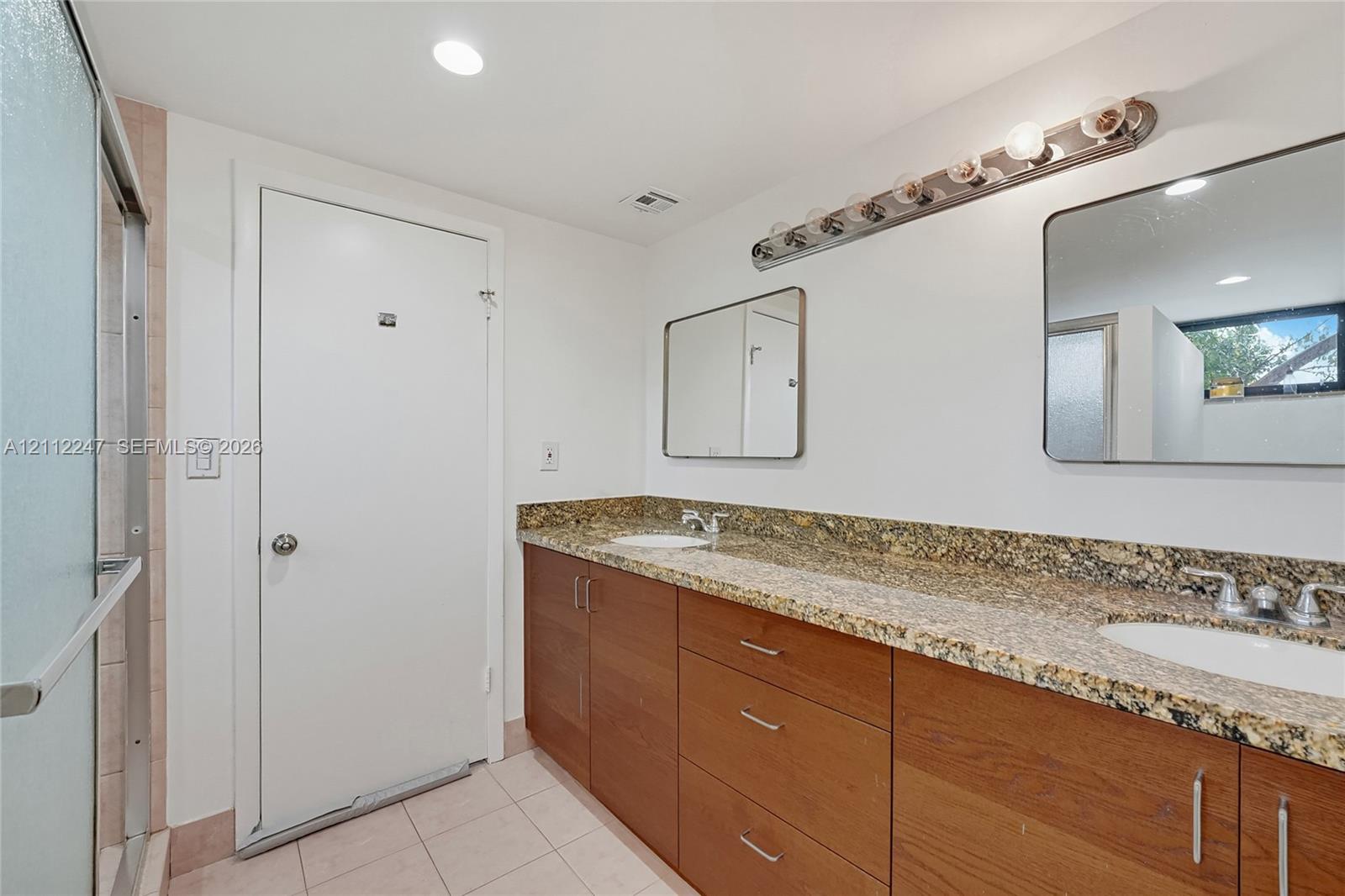 Dual-sink vanity with stone countertops, wooden cabinetry, two wall-mounted mirrors, and tiled flooring