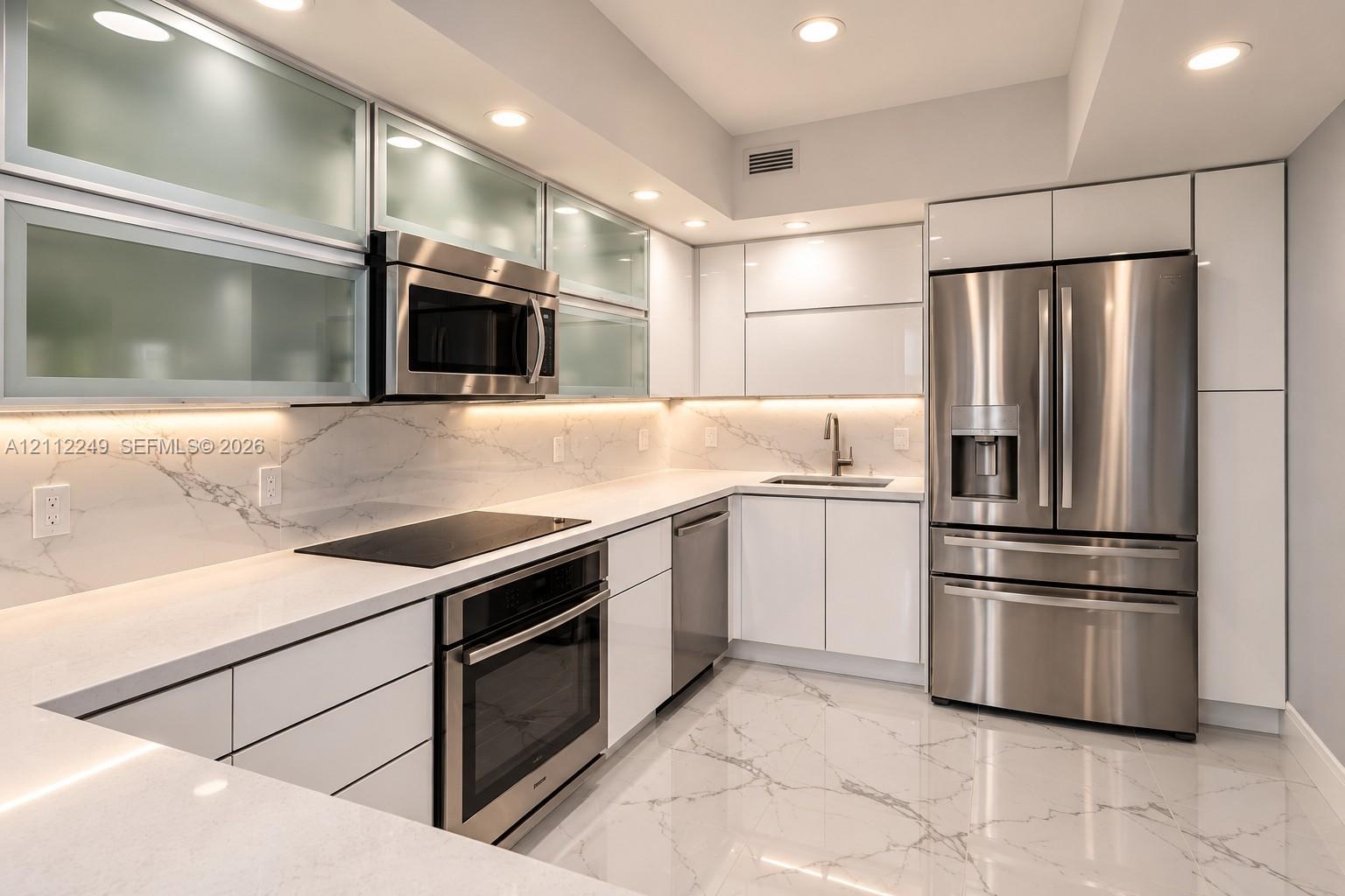 Modern kitchen featuring high-gloss cabinetry, upper glass-front display cabinets, stone-surfaced countertops, integrated under-cabinet lighting, and stainless steel appliances