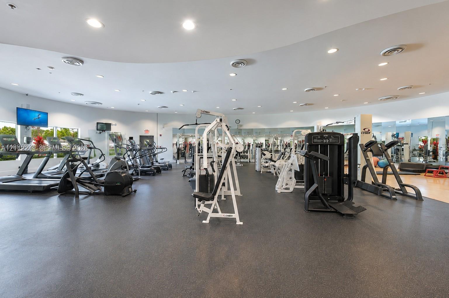 Fitness center featuring a curved ceiling design, recessed lighting, expansive wall-to-wall mirrors, rubberized flooring, and multiple built-in ventilation registers