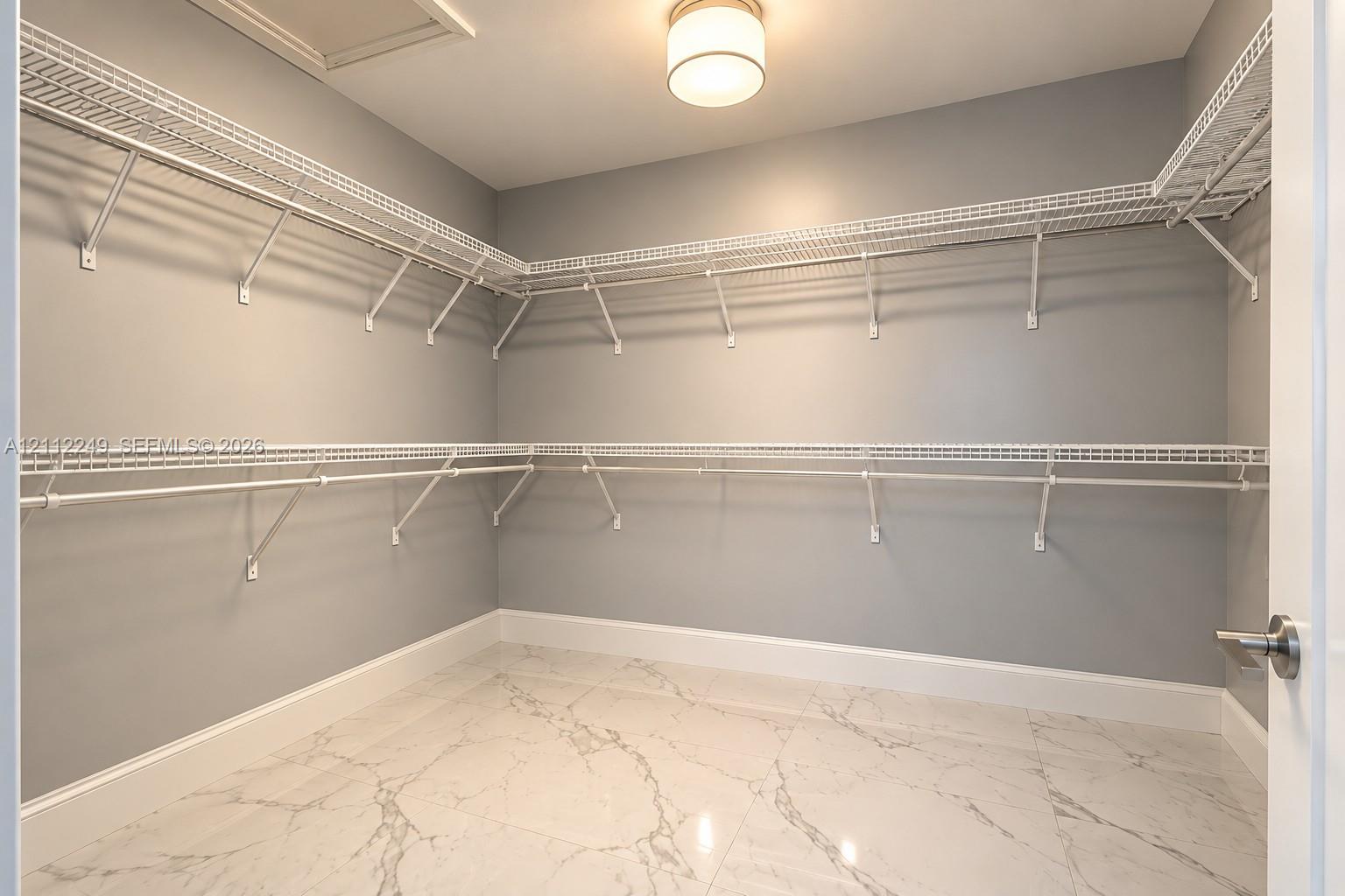 Walk-in closet featuring large-format tile flooring with a veined pattern, multi-tiered white wire shelving, and a flush-mount drum ceiling light fixture
