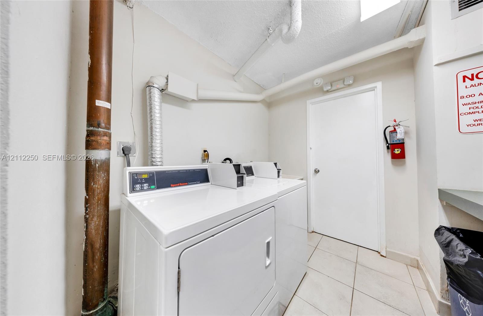 Laundry facility featuring coin-operated appliances, white tiled flooring, and a solid-core interior door