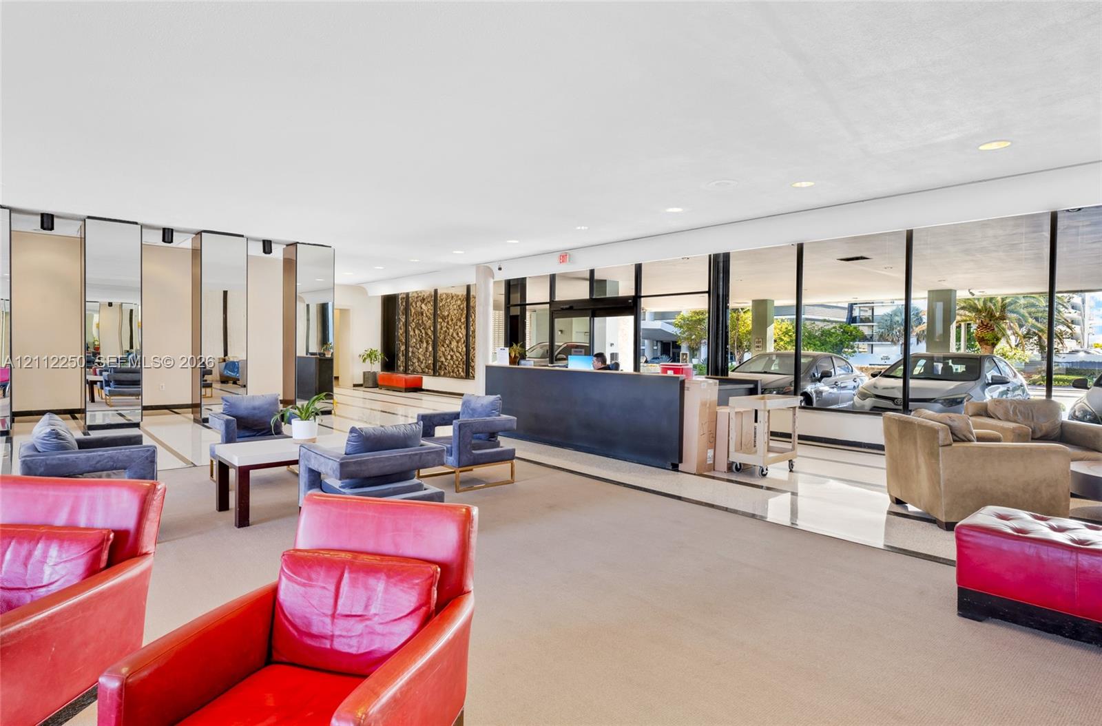 Expansive lobby featuring floor-to-ceiling glass paneling, full-height mirrored wall panels, polished stone flooring, and a built-in reception desk