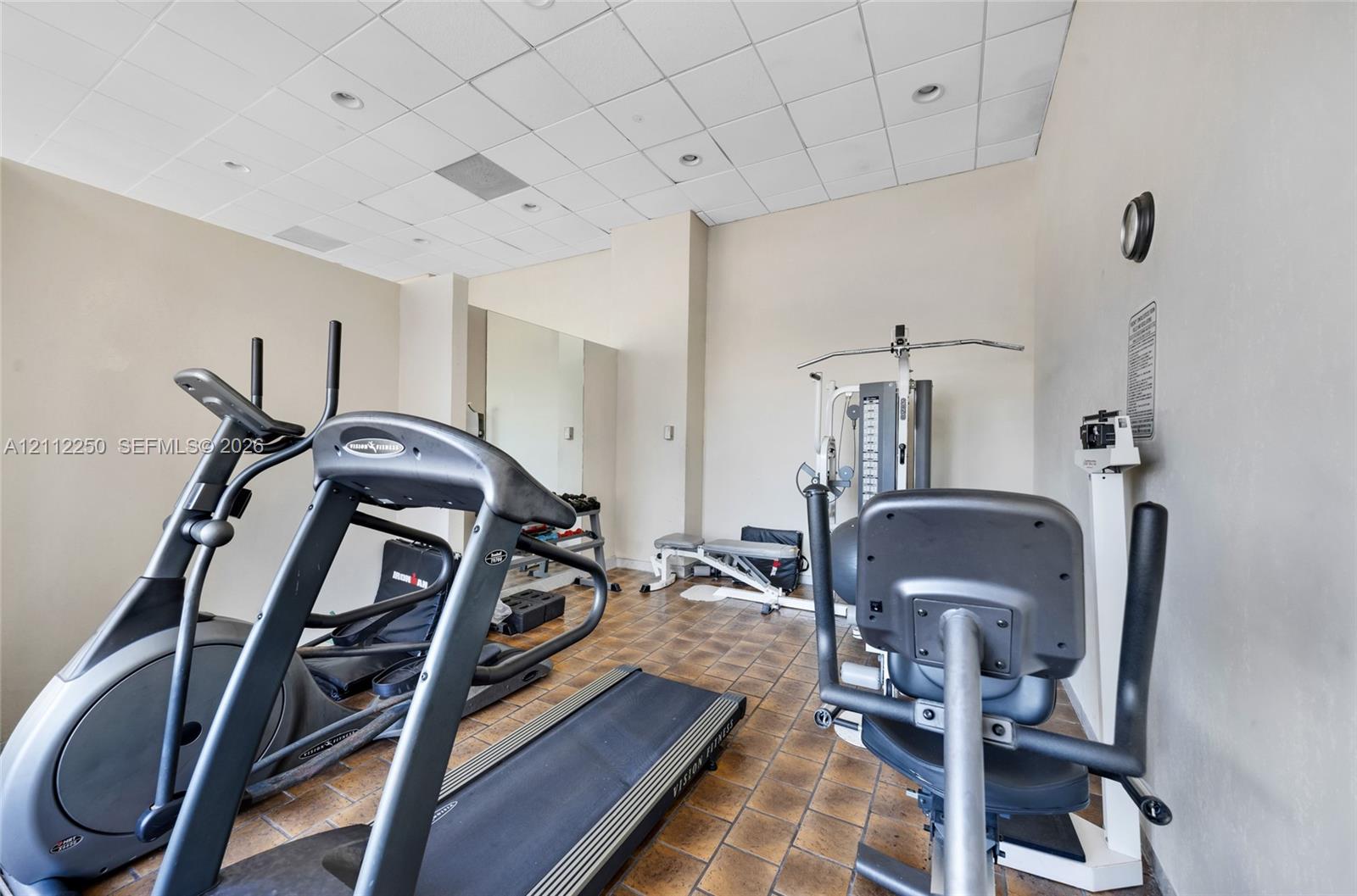 Fitness space featuring ceramic tile flooring, recessed ceiling lighting, drop ceiling panels, and wall-mounted mirror